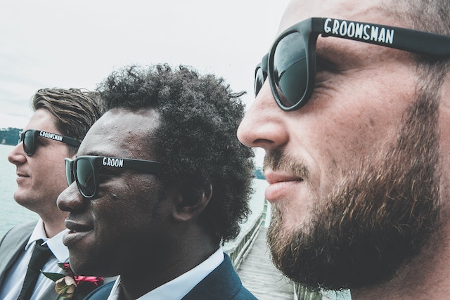 Picking Out Suits and Attire for the Groom and Groomsmen: 
Stylish multiethnic groom and groomsmen standing on embankment and smiling on wedding day.
